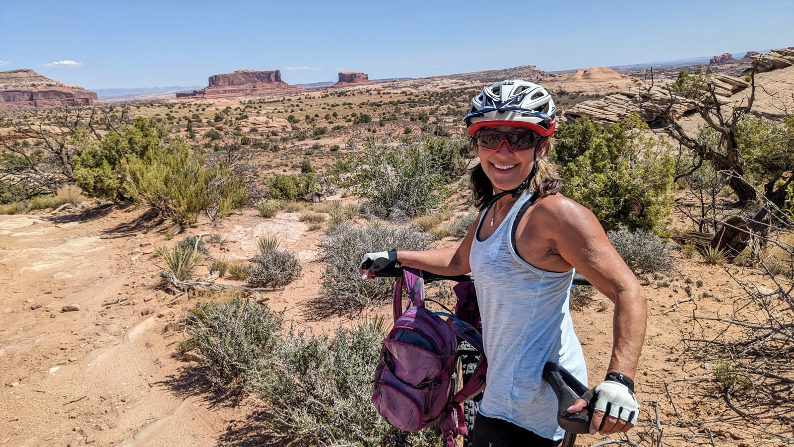 Alisa Geller with her mountain bike above a red-rock canyon trail near Moab, grinning under a white helmet